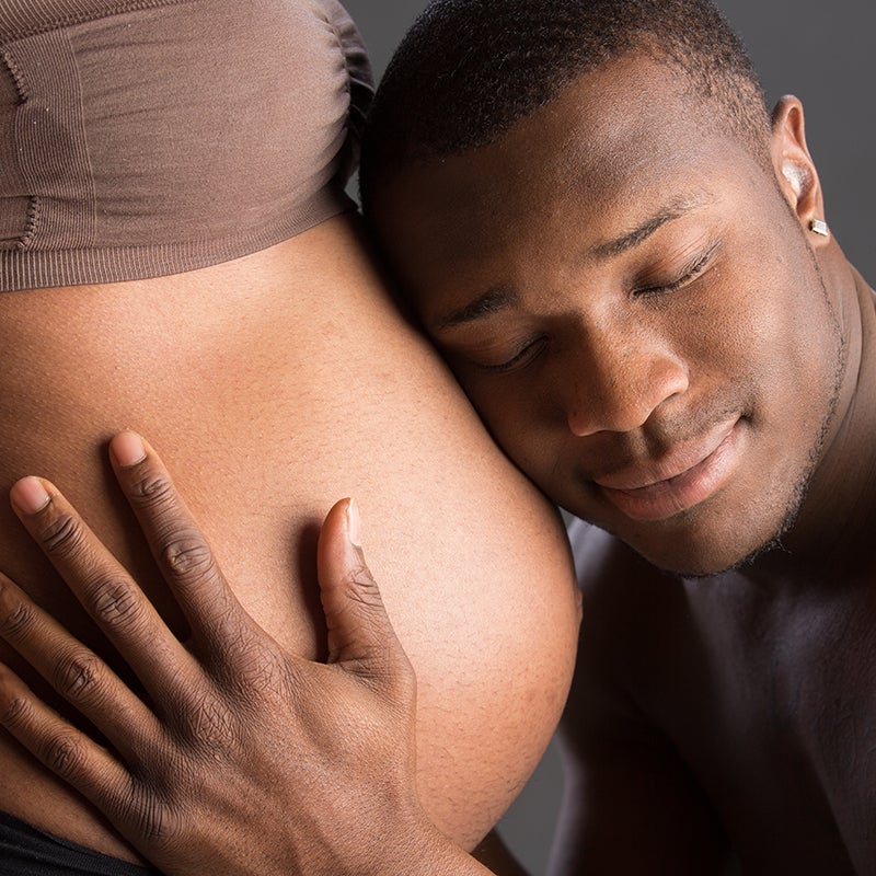 man with ear to woman's pregnant belly